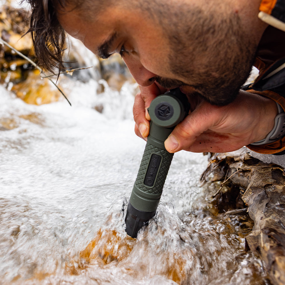 Person using a water filter straw drinking from a stream