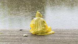 A person in a yellow rain poncho sitting on a dock at a lake.