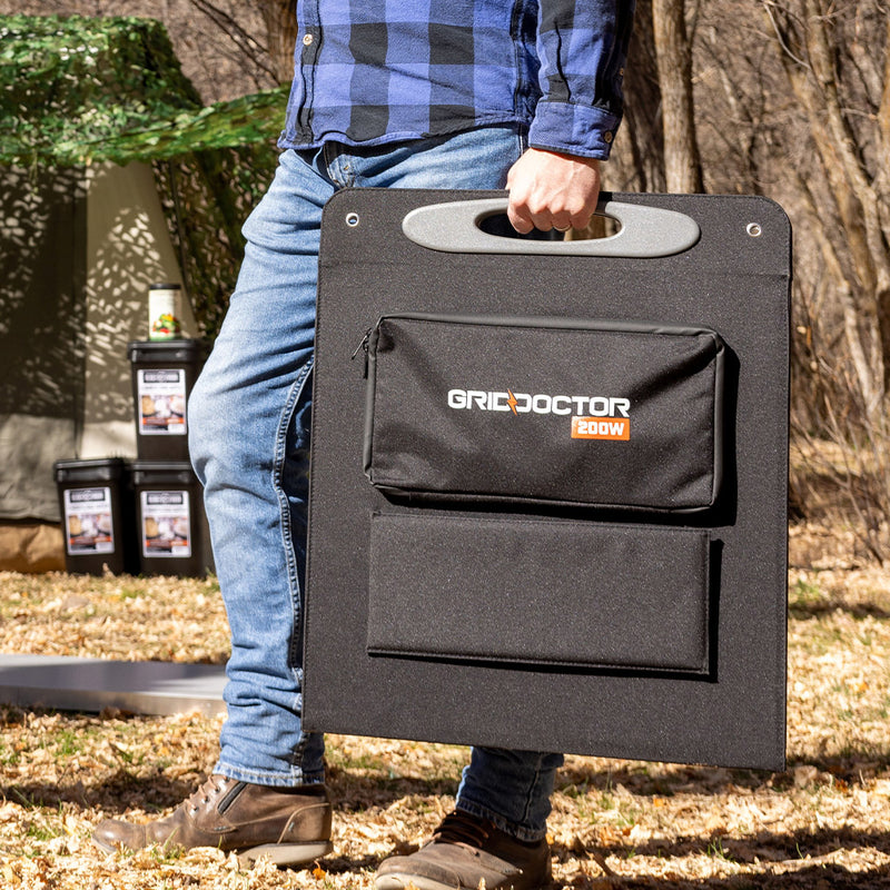 Man carrying the Grid Doctor solar panel kit in its protective case, walking outside with a backdrop of trees, demonstrating the kit's portability and ease of transport in outdoor settings. (7340716949644)