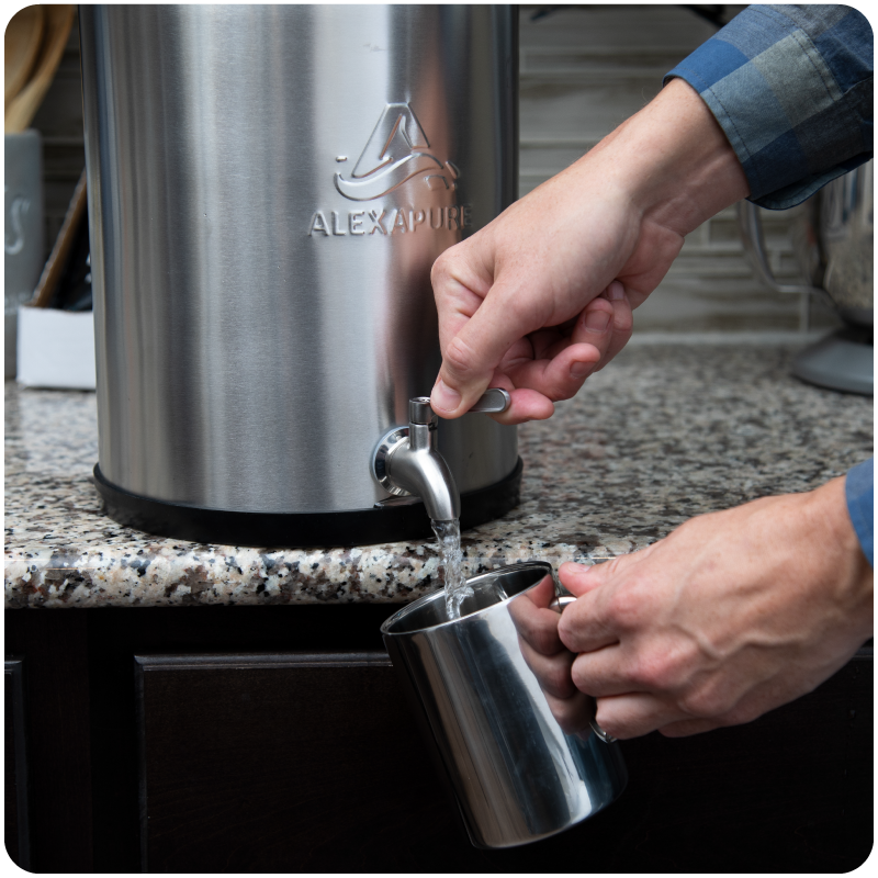 Hands turning the spigot of the AlexaPure Pro to pour water into a metal cup