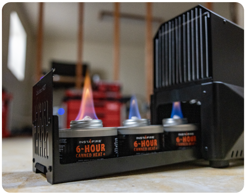 InstaFire 6-Hour Canned Heat portable camping stove system with three lit canisters, shown on a tabletop in a workshop setting.