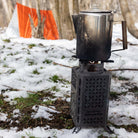 InstaFire Inferno Outdoor Biomass Stove cooking a kettle outdoors in the snow with orange emergency tent in the background