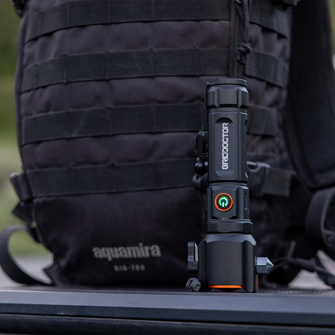 Tactical Flashlight by Grid Doctor shown in front of a backpack.