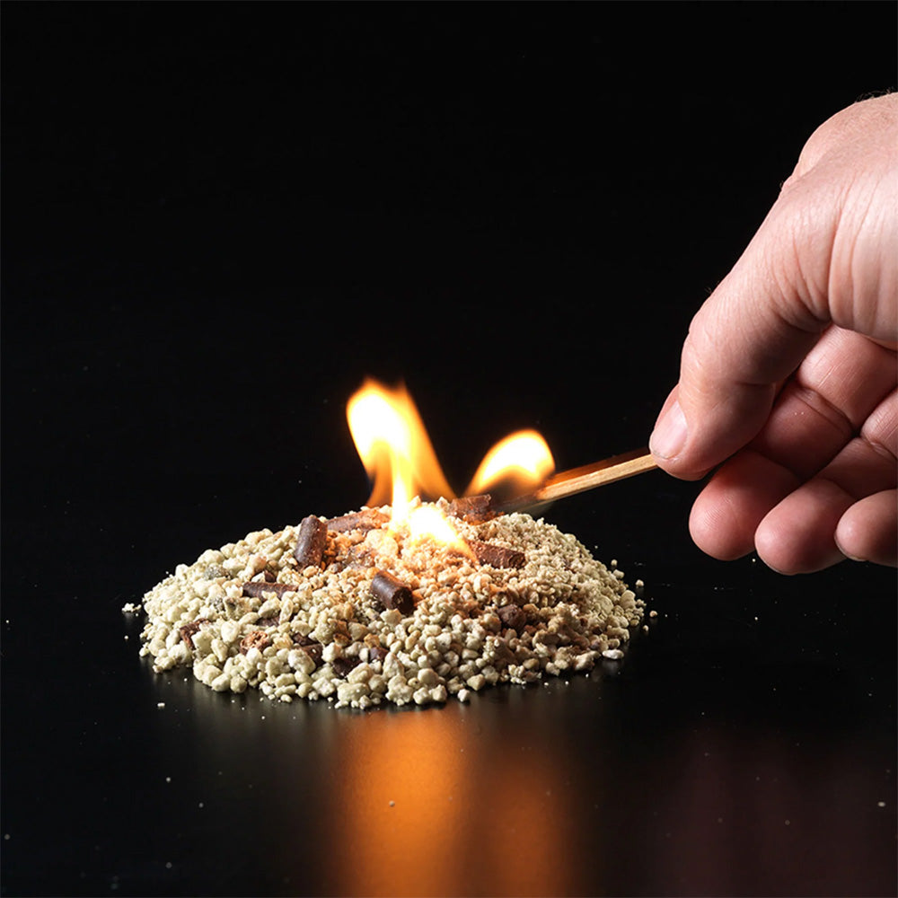 Hand adding InstaFire Fire Starter & Fuel granules to a small burning pile to demonstrate fire-starting use.