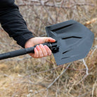 Hand holding a black folding shovel