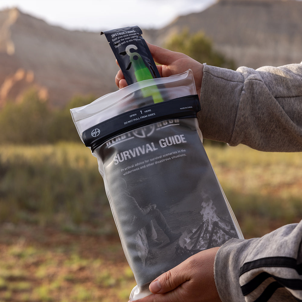 Person holding a survival guide and glowstick in a waterproof package